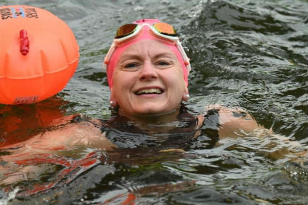 Open water swimmer wearing Snake & Pig pink goggles on her head and using an orange safety buoy