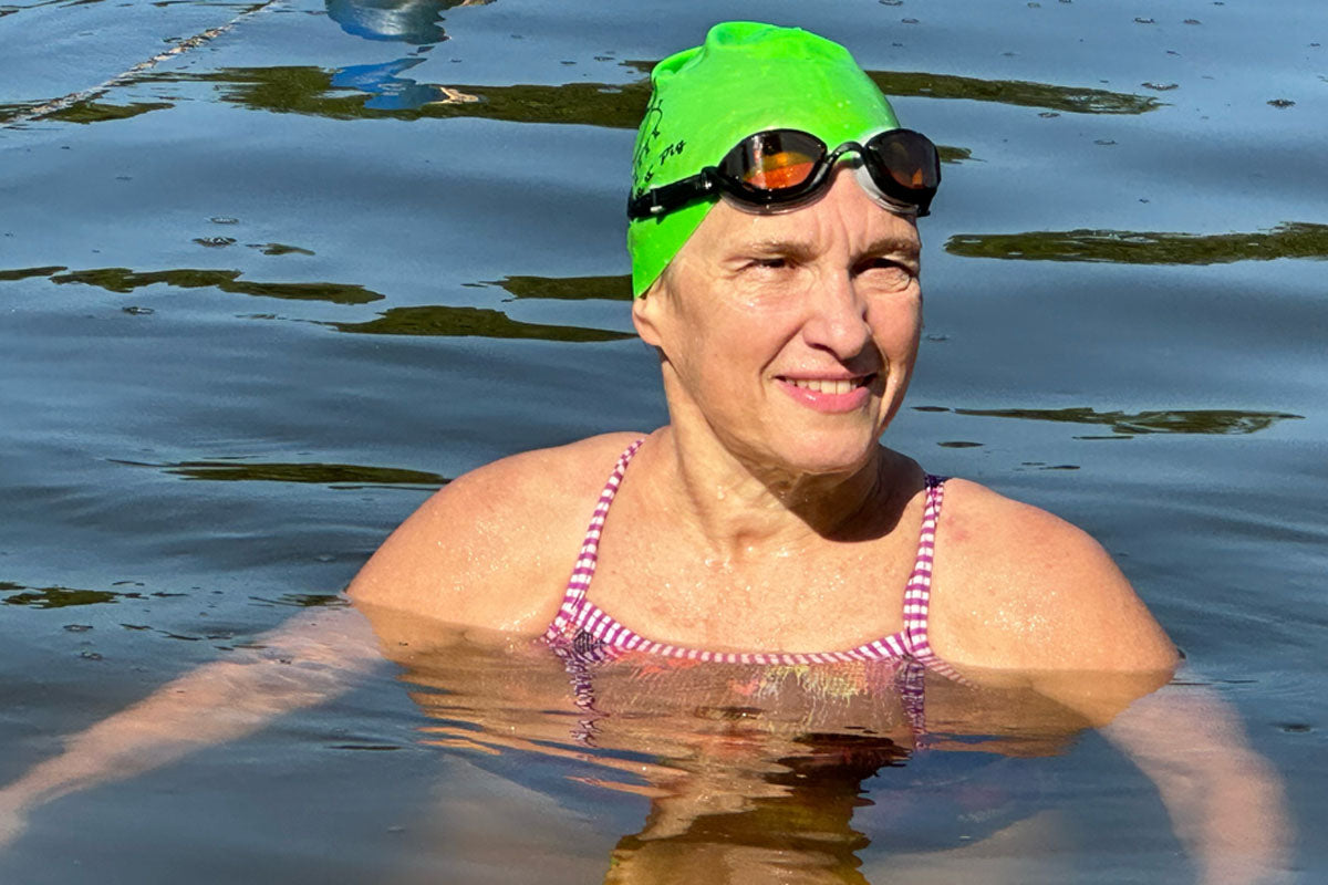 A woman floats in a lake while wearing amber lens goggles and a green swim cap