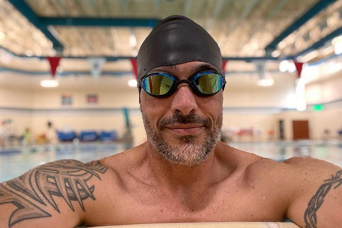 A bearded masters swimmer in an indoor pool with a black swim caps wears Snake & Pig goggles to avoid raccoon eyes