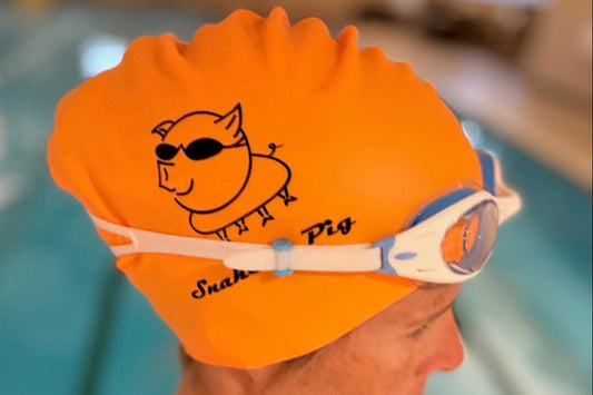 Woman wearing orange long-hair cap with junior Basilisk goggles at an indoor pool