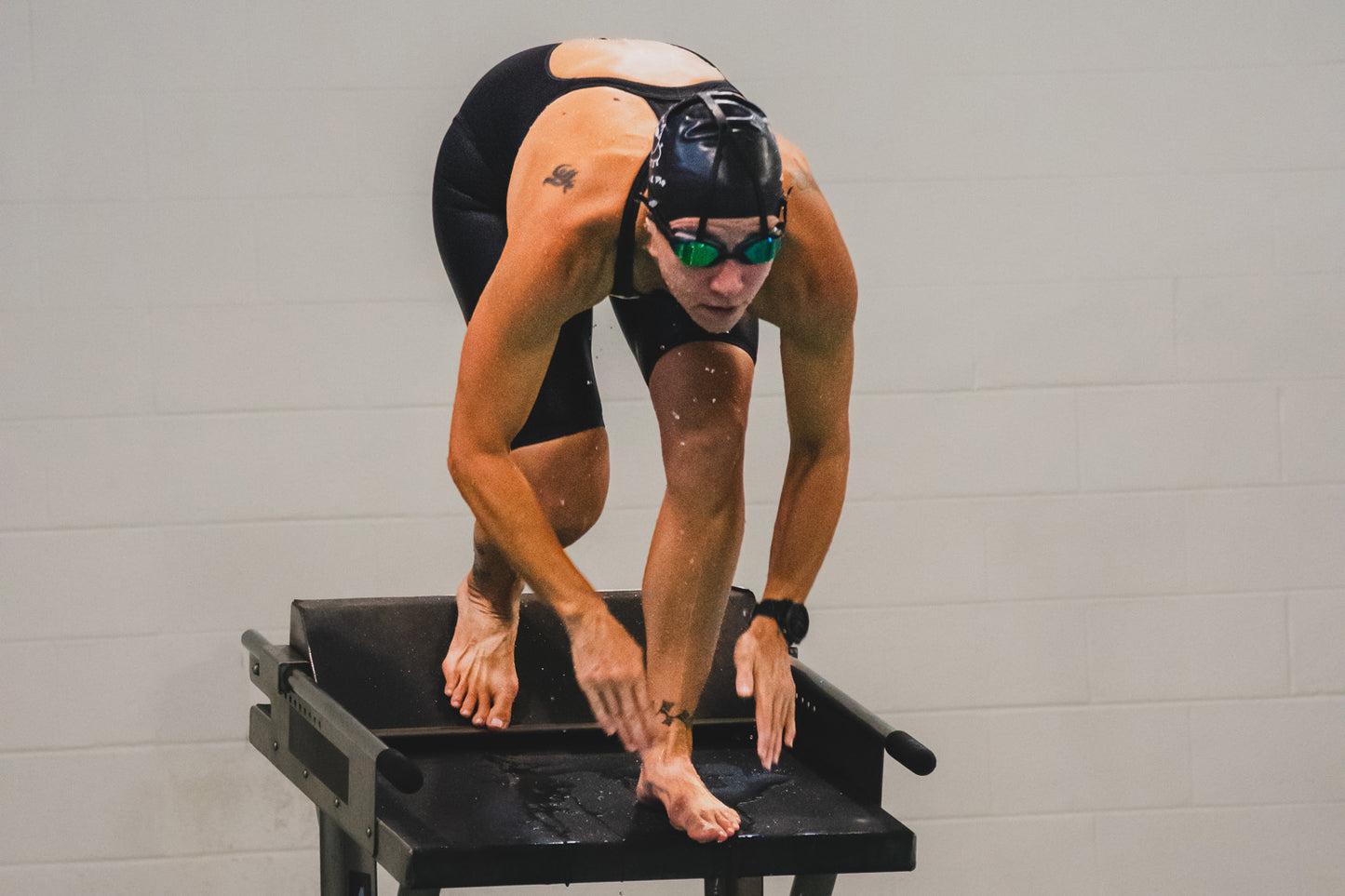 A swimmer prepares to dive off the blocks with a pair of Snake & Pig's top anchor goggles on