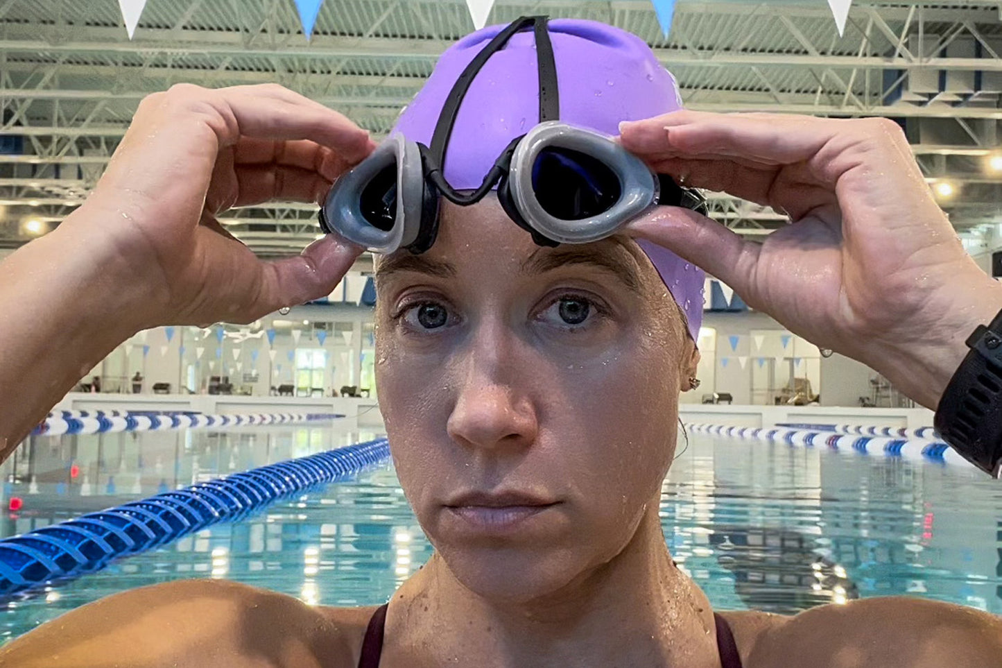A swimmer at an indoor pool flips up the lenses of a pair of top anchor goggles, revealing her eyes