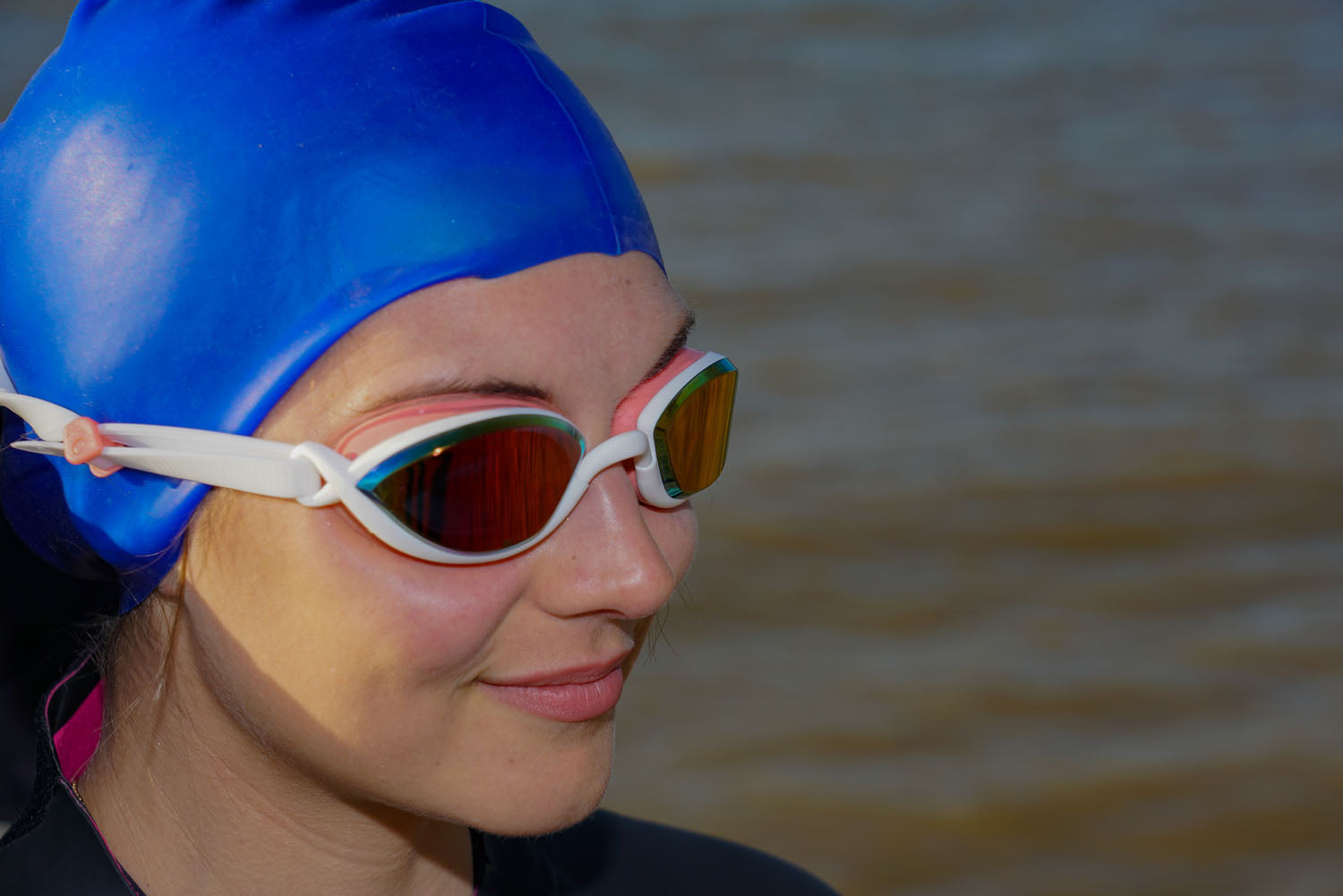 Triathlete wearing a blue cap and pink Snake & Pig goggles at a lake
