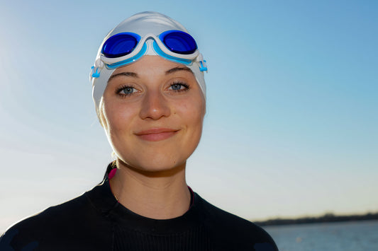 A woman in a wet suit wears blue tinted goggles on her forehead over a white swim cap