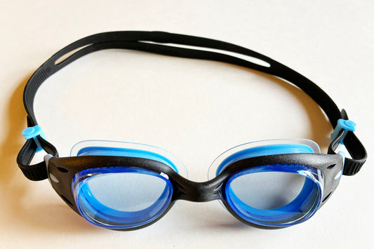 Black and blue Basilisk Junior swim goggles with light blue lenses on a white background
