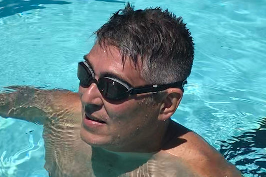 A man in a swimming pool wears amber goggles in bright sunlight